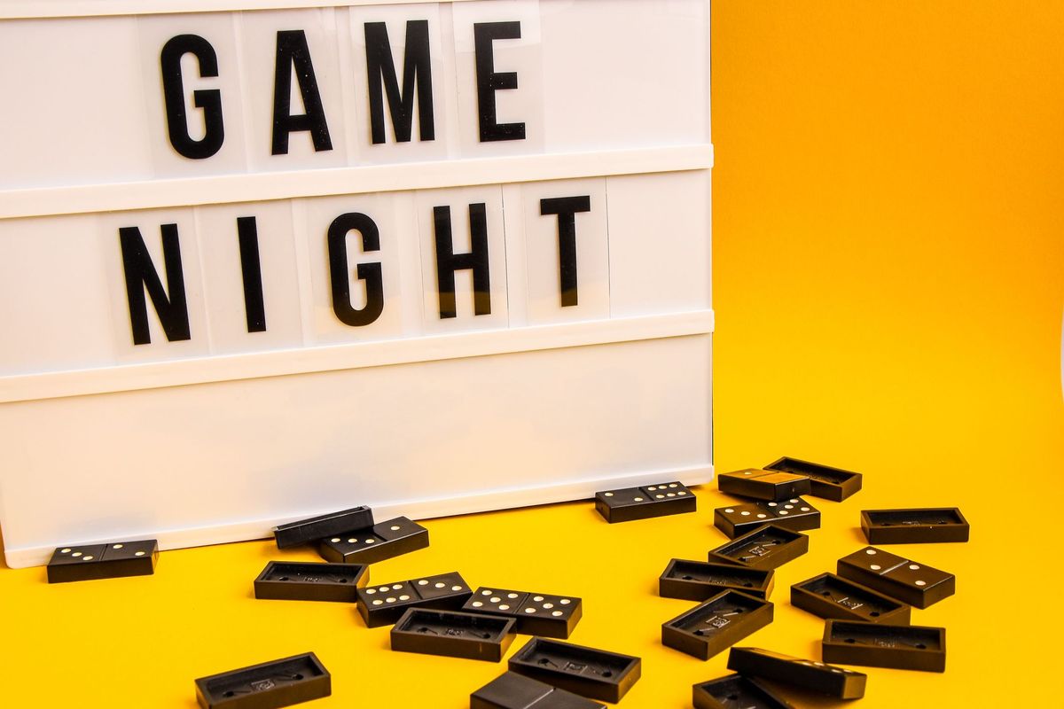 Spieleabendtext auf Leuchtkasten mit schwarzen Dominosteinen auf gelbem Hintergrund, Tischspiel