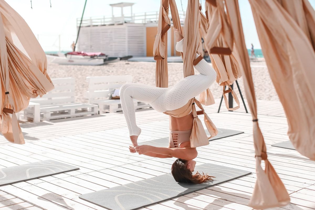 Çimərlikdə dəniz kənarında antiqravitasiya yoga ilə məşğul olan gözəl bir qadın